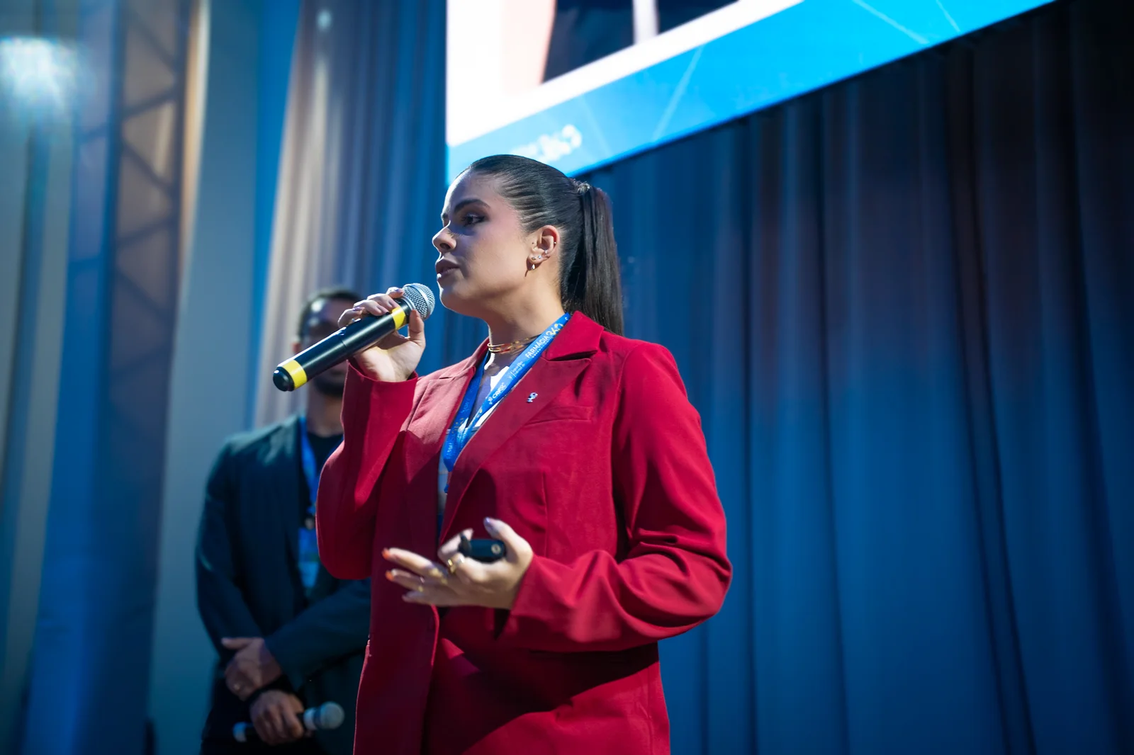 Bianca Balbino falando ao microfone em um evento de farmácia em Balneário Camboriú